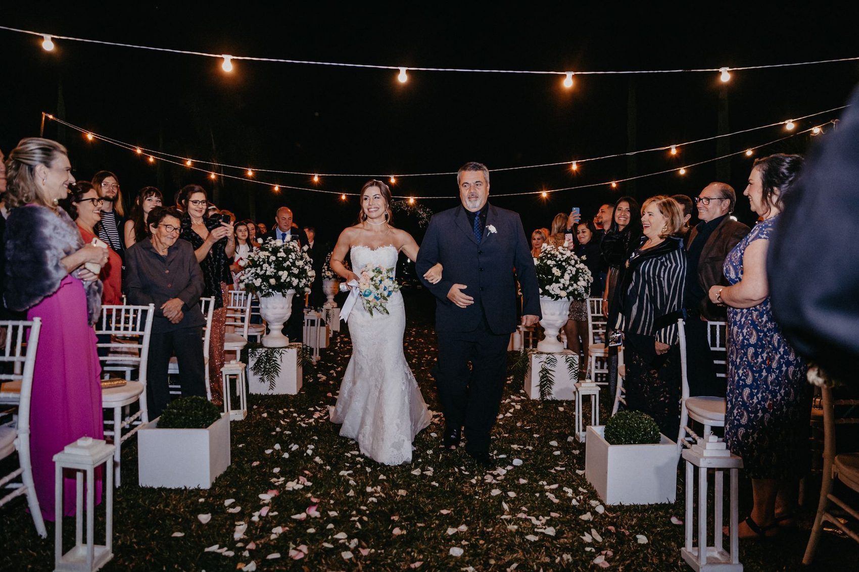 A bride walking down an aisle lit by hanging lights
